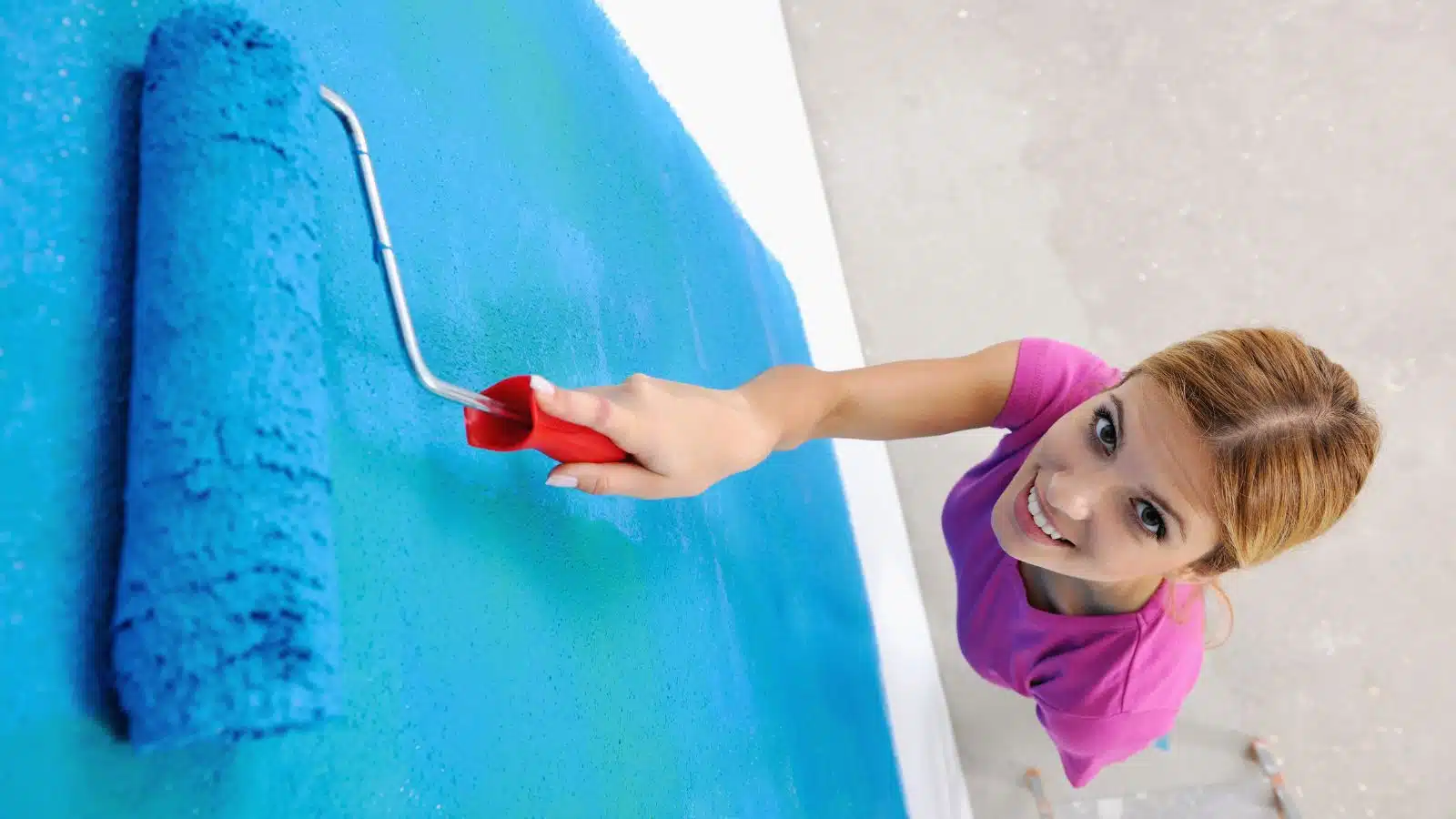 overhead angle of a woman painting a wall bright blue
