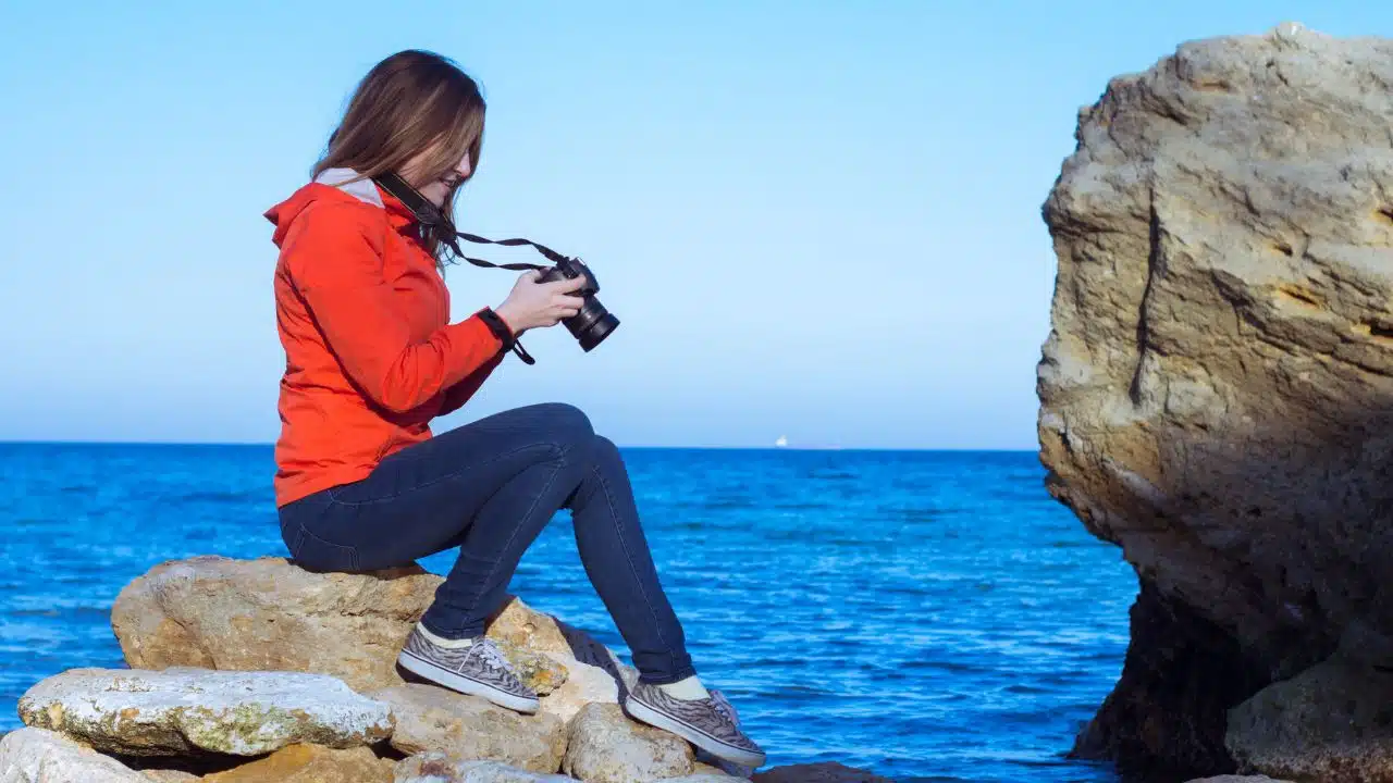 Young woman with dslr photo camera taking pictures near the ocean