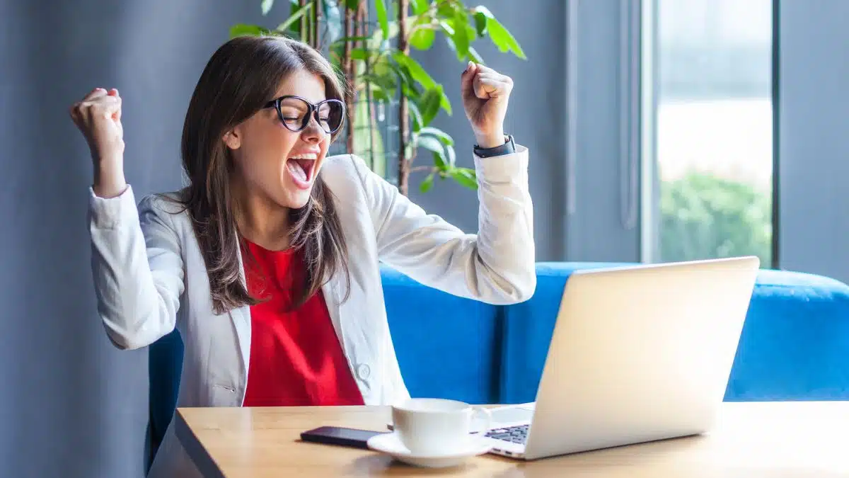 excited business woman at desk with laptop reading good news