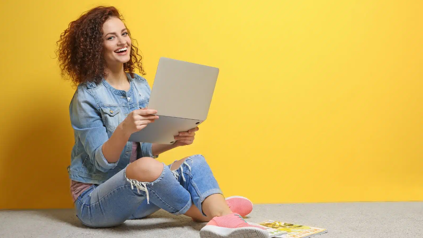 young woman using a laptop on a yellow background