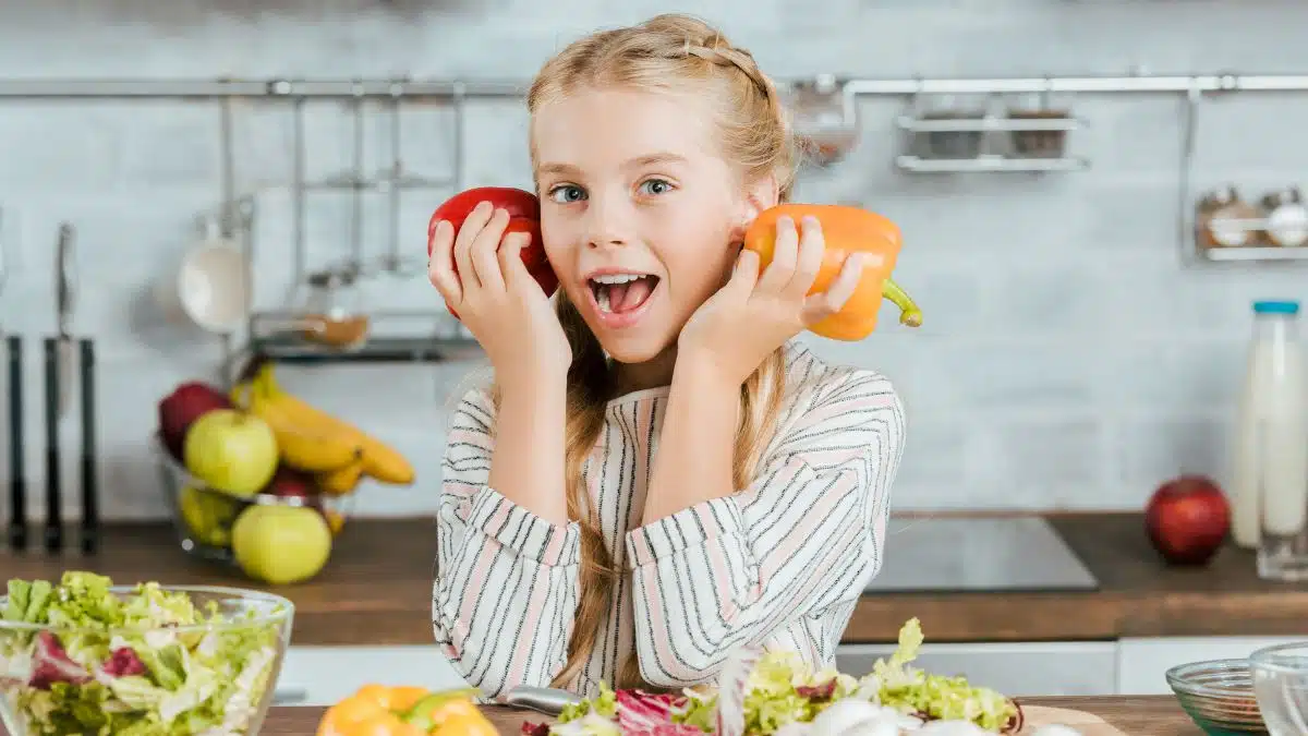 smiling young girl playing with veggies while cooking