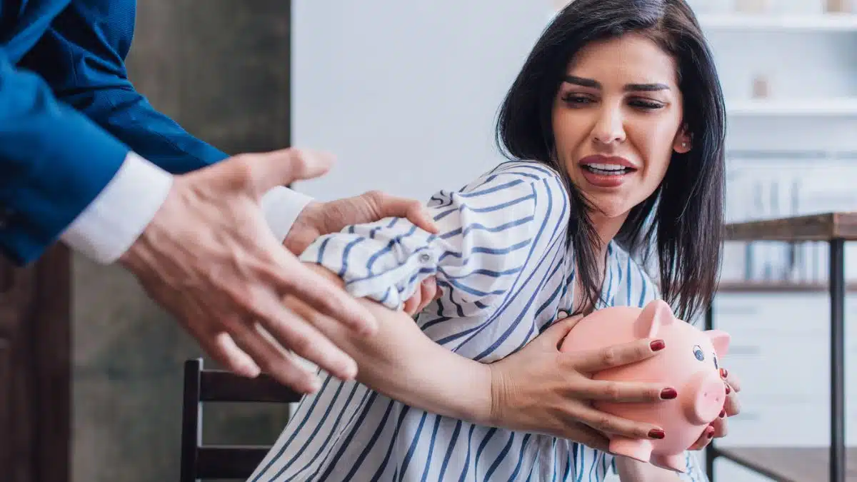 debt collectors hands trying to take a piggy bank of money from a woman