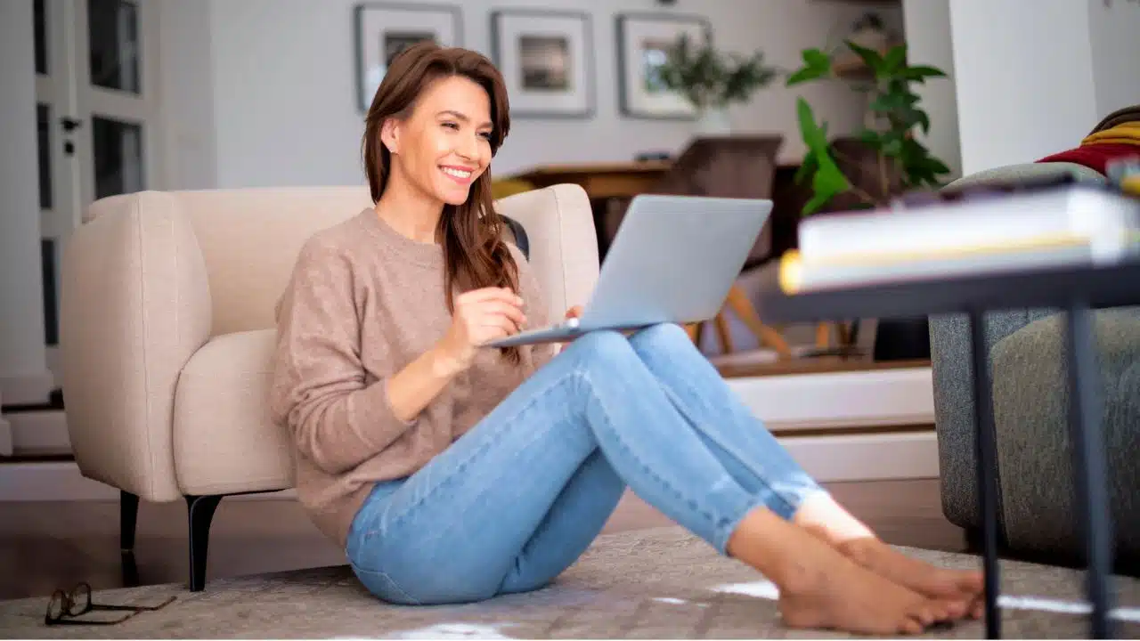 happy woman with her laptop sitting on the living room floor
