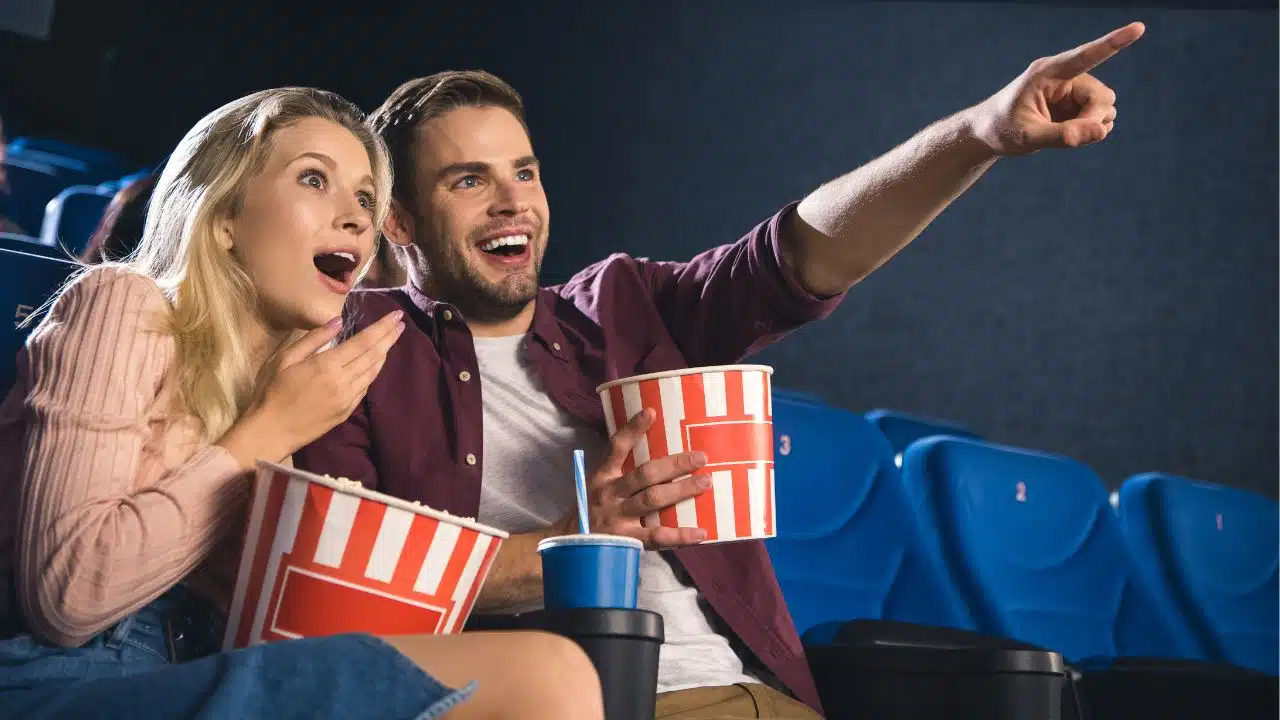 Shocked couple with popcorn and soda watching film together in a movie theatre