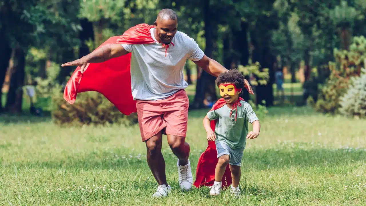 father and son dressed as superheroes running in a park