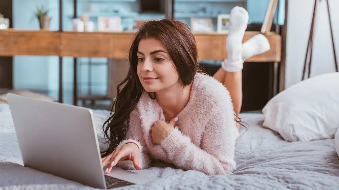 woman working on laptop laying on her bed