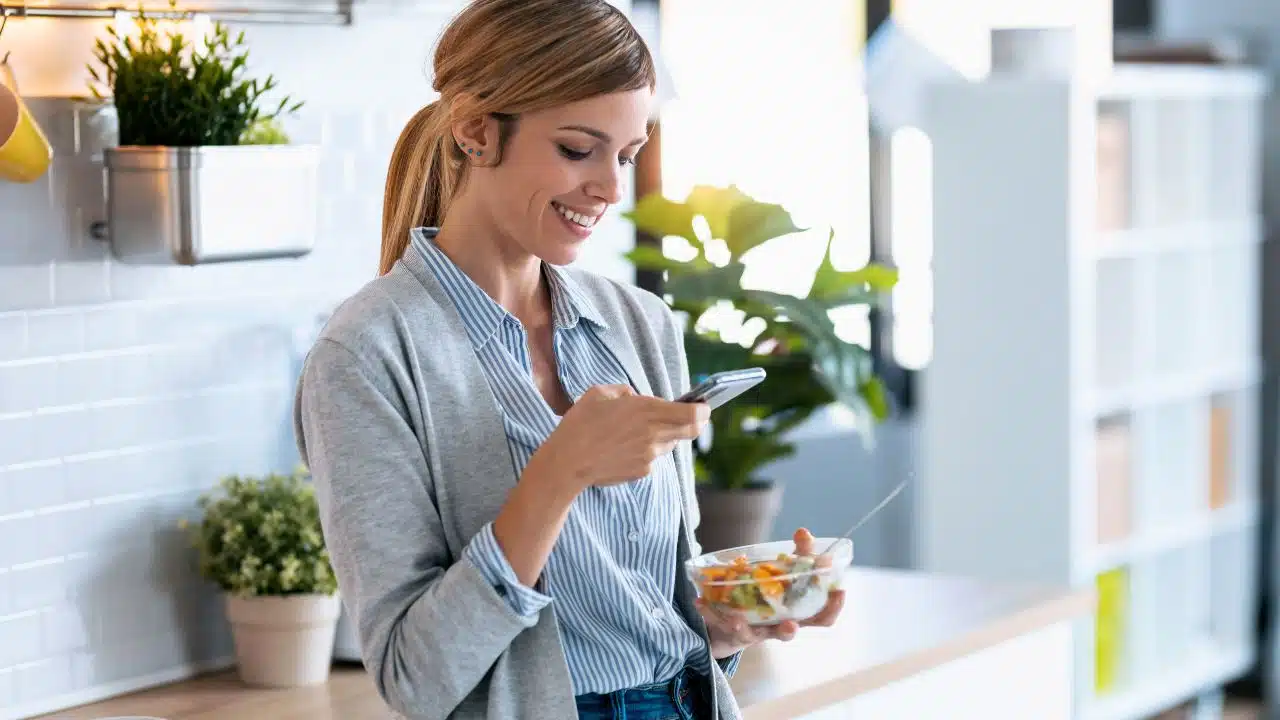 woman looking at her phone eating snack in break room