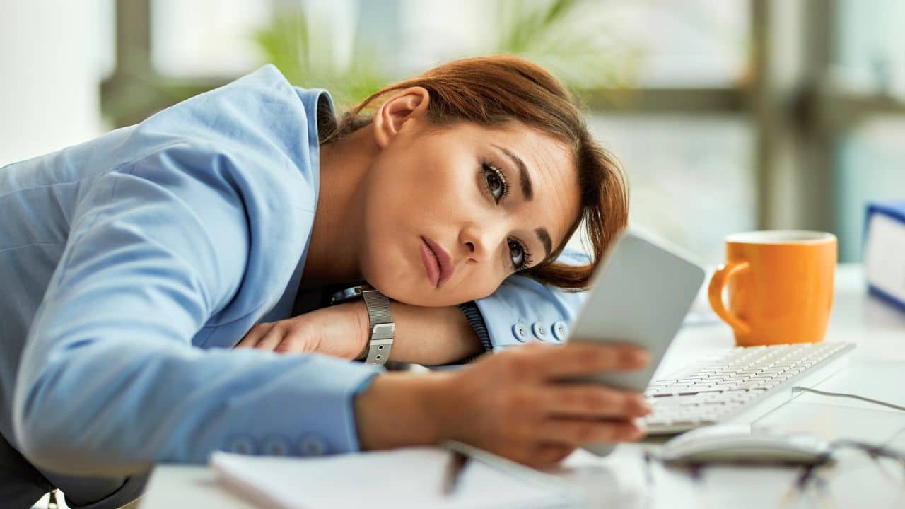 exhausted woman resting at her desk on her phone