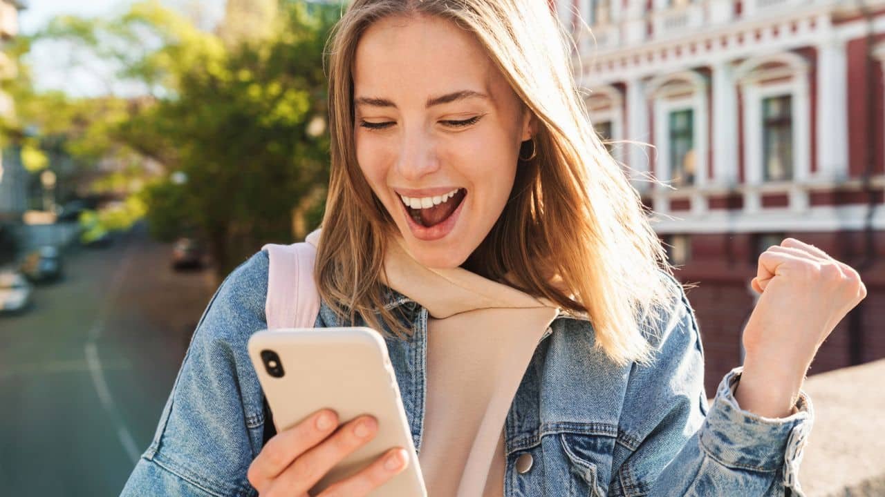 cheerful woman outside looking at cell phone, getting good news