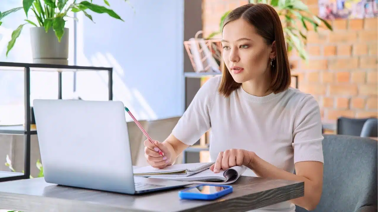 woman with paperwork and laptop writing in notebook